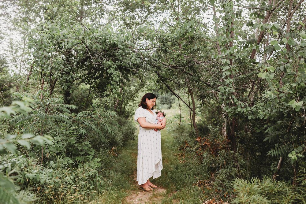 Mother and newborn standing outside under and arbor of trees